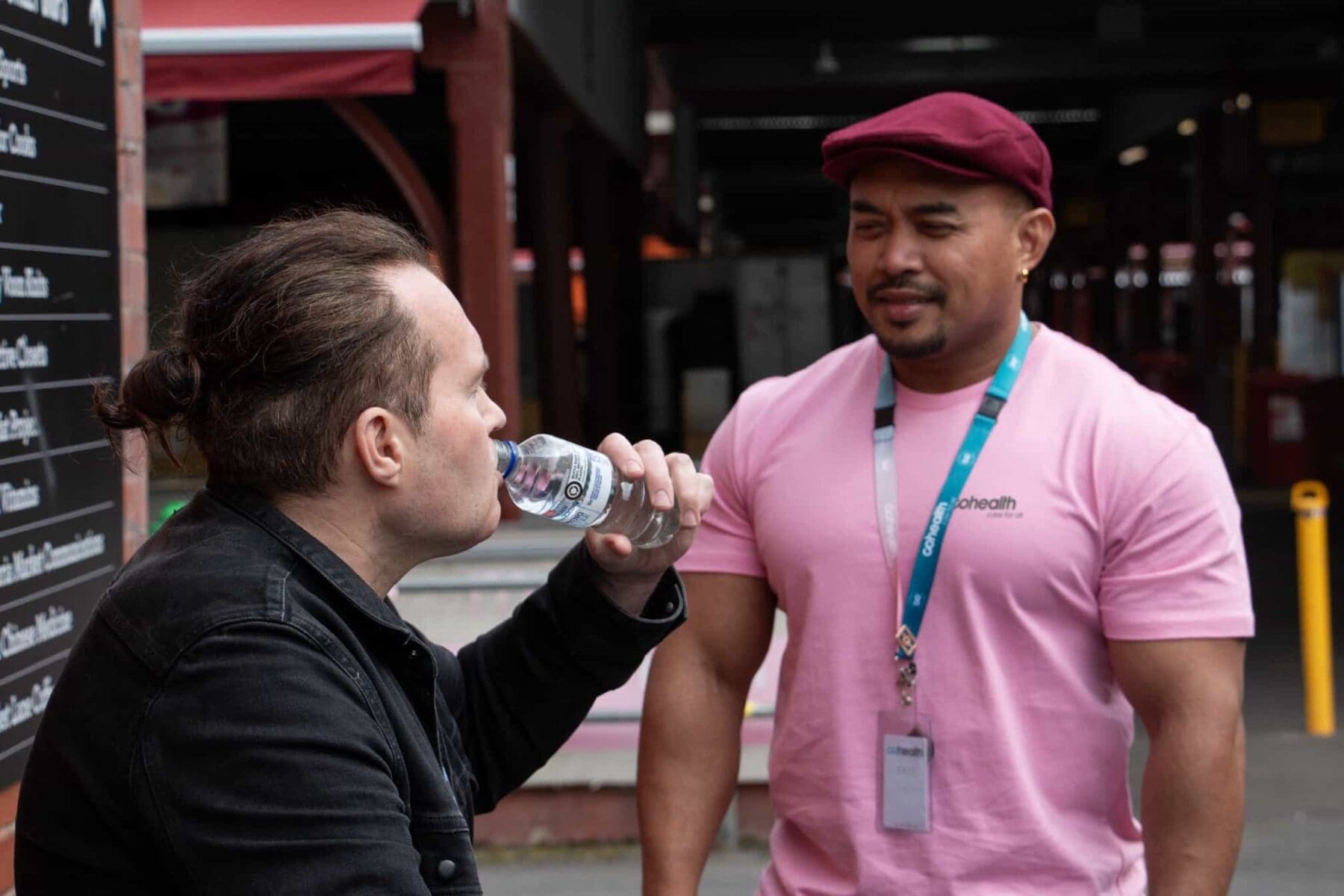 A member of cohealth's Public Intoxication Response Service team wearing a pink shirt and standing by somebody drinking from a water bottle